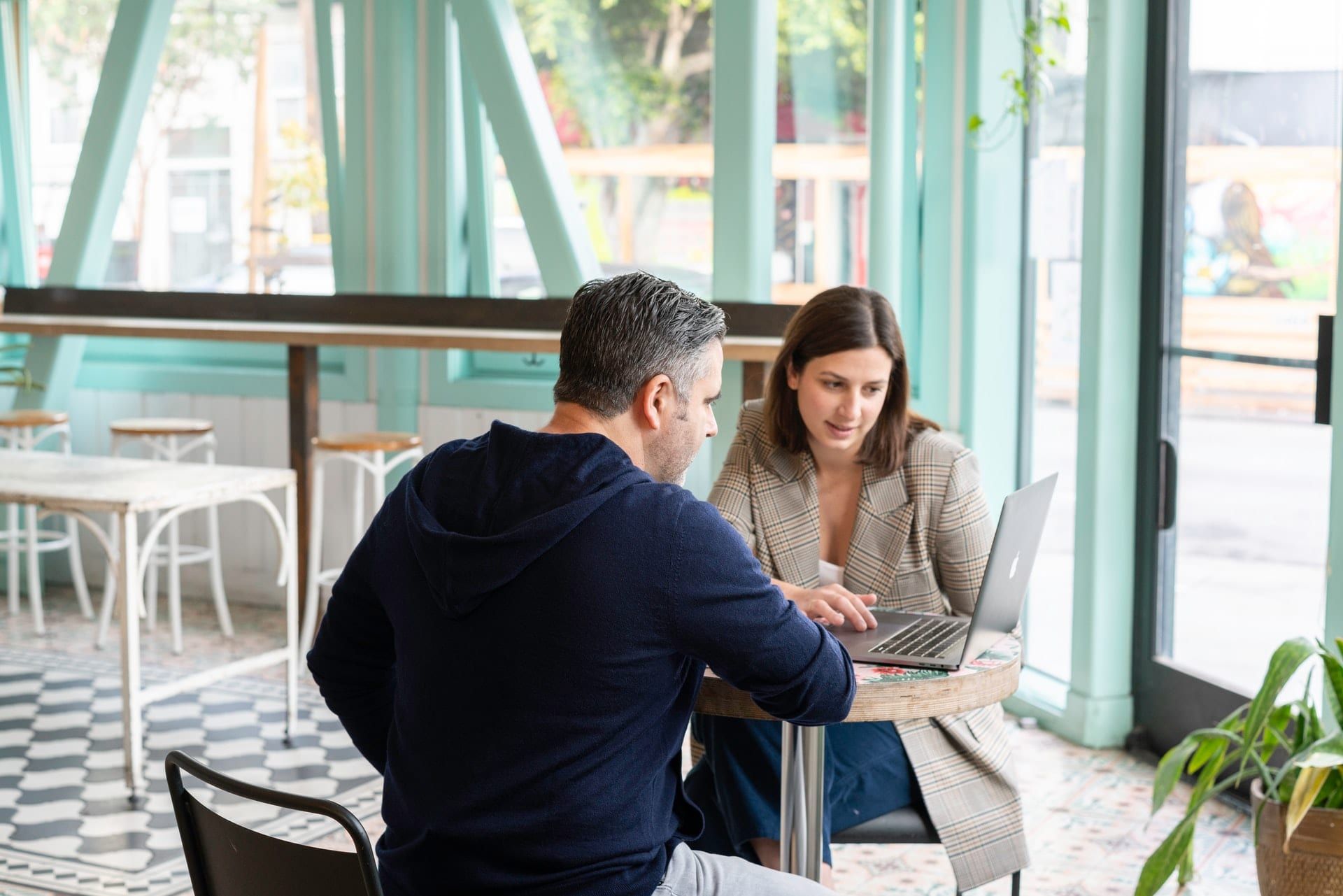 A man and a woman going through something on a laptop at a café table