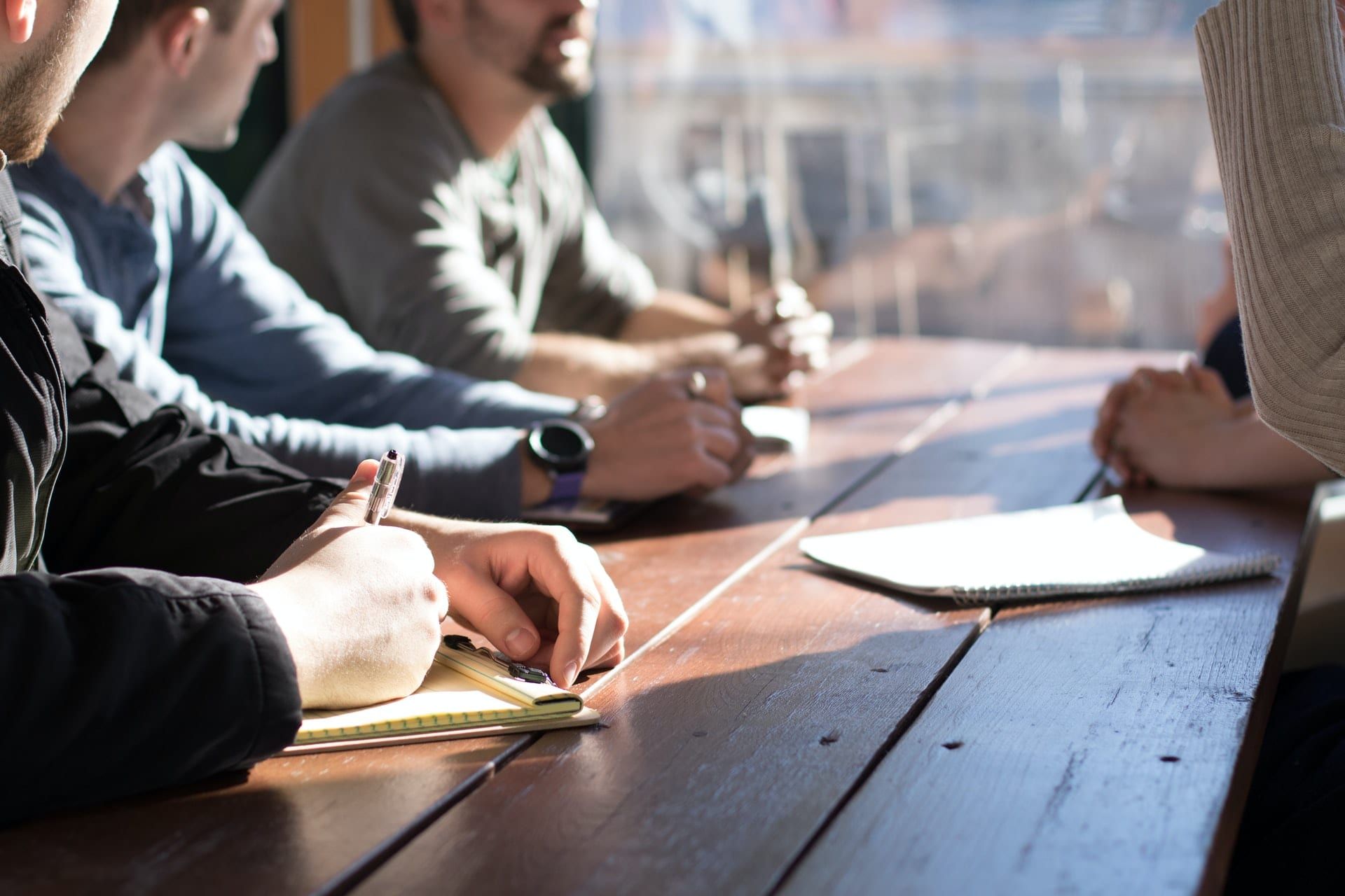 Colleagues at a long table taking notes in their notebooks